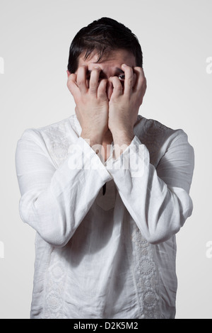 Young man hiding his face with hands while looking through fingers Stock Photo