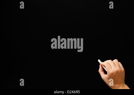 Hand writing something with white chalk on a blank blackboard. Stock Photo