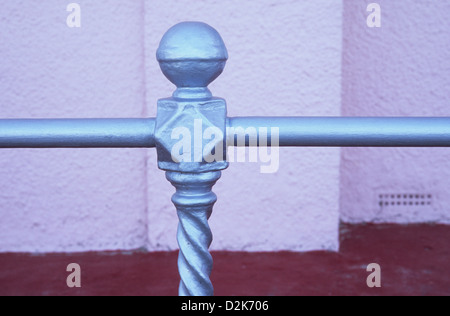 Detail of ornate silver painted railings with knob in front of pale pink pebbledashed wall and red concrete floor Stock Photo