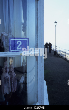 Bay window with continental enamel sign stating 2 overlooking promenade with figures and railings and sea Stock Photo