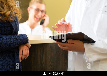 Patient and doctor in reception area of office of doctor or dentist, he holds a clipboard, the receptionist is on the phone Stock Photo