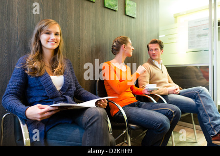 Female patient at reception of clinic looking at the viewer, in the background other people waiting for her treatment Stock Photo