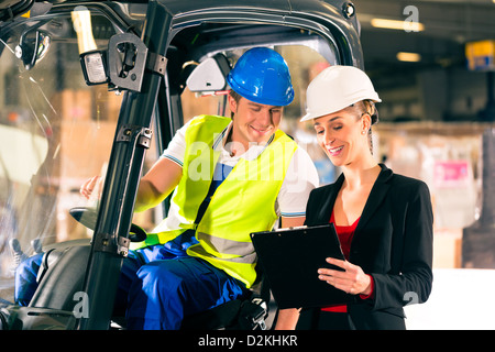Forklift driver and female super visor with clipboard at warehouse of freight forwarding company Stock Photo