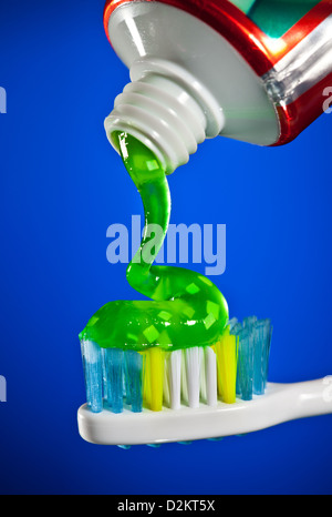 toothpaste being squeezed onto a toothbrush on a dark blue background Stock Photo
