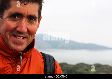Close up of an rugged middle aged man with brown hair looking at the camera smiling.  Outdoors with the bay in the background. Stock Photo