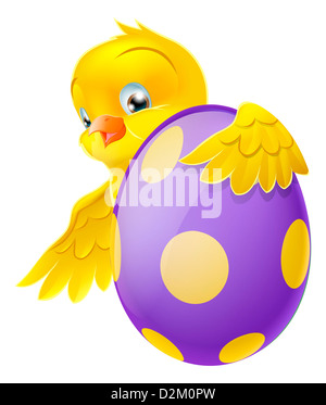 Cute Easter chick cartoon character holding onto and peeking round a painted chocolate Easter egg Stock Photo