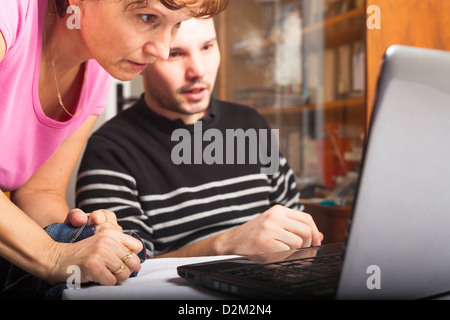 Middle aged woman and young man using laptop at home. Stock Photo