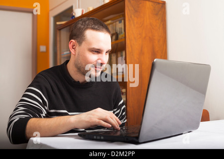 Young smiling man using laptop at home. Stock Photo