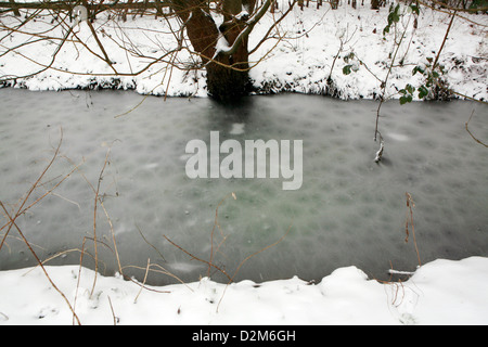 Frozen ditch water in a flood plain, Kidlington, Oxfordshire, England. Snow is falling and lays on the ground. Stock Photo