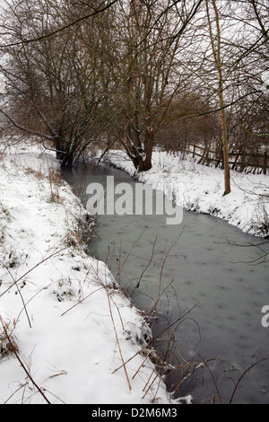 Frozen ditch water in a flood plain, Kidlington, Oxfordshire, England. Snow is falling and lays on the ground. Stock Photo