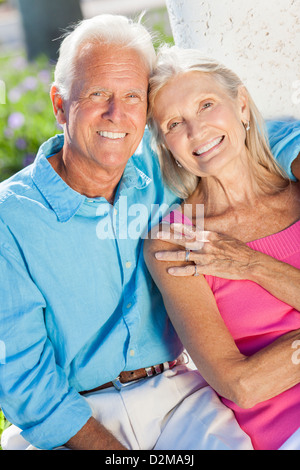 Happy senior man and woman couple sitting together outside in sunshine smiling Stock Photo