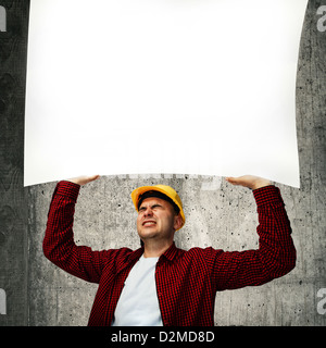 Construction worker with yellow hard hat in red shirt holding a whiteboard above his head. Stock Photo
