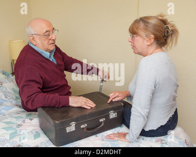 elderly man sat on bed with suitcase in discussion with daughter Stock Photo