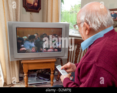 elderly man watching television at home using television remote control to change channels Stock Photo