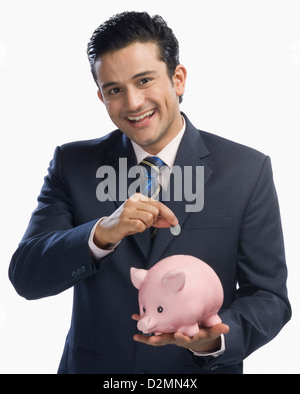 Businessman putting a coin into a piggy bank Stock Photo