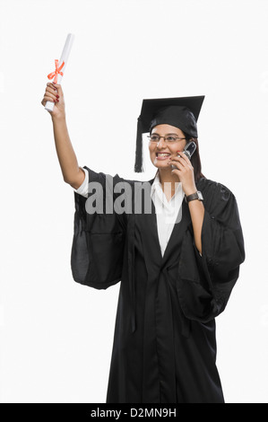 Graduate woman talking on a mobile phone and holding her diploma Stock Photo