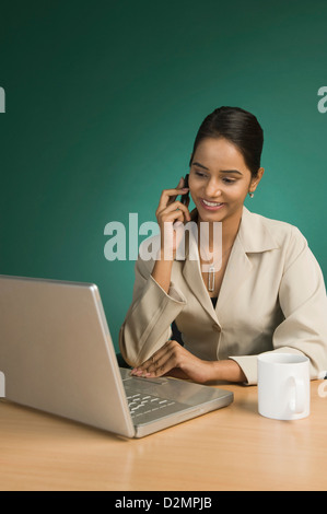 Businesswoman using a laptop and talking on a mobile phone Stock Photo