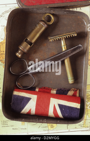Tobacco tin lying on map and containing brass whistle razor scissors and folded Union Jack flag Stock Photo