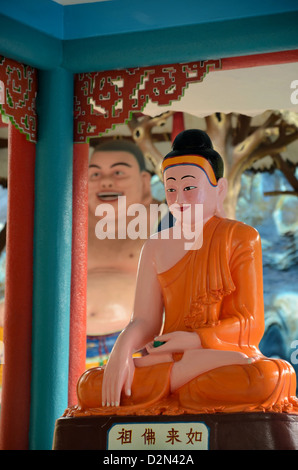A ceramic statue of a saffron robed meditating Buddha in a lotus Singapore. Note the laughing Buddha monk in the background. Stock Photo