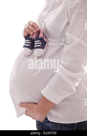 Pregnant woman keeping baby-shoes. Close up shot of belly and shoes. Stock Photo