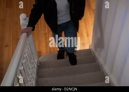 Young male wearing jeans and a black jacket and a teeshirt walking upstairs alone (face not shown). Stock Photo