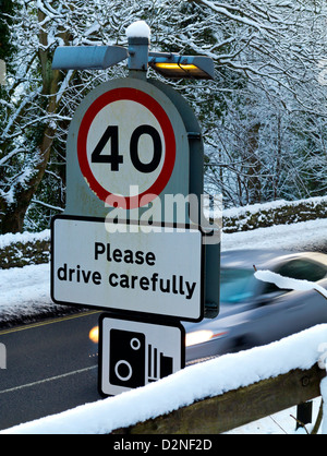 40mph and Please Drive Carefully sign with speed camera warning symbol on winter road with car behind Derbyshire UK Stock Photo