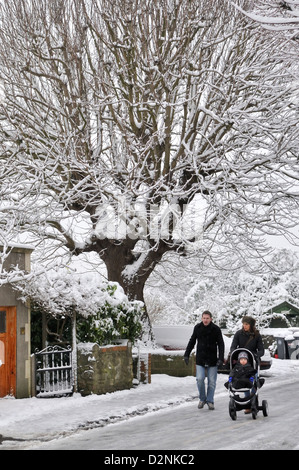 Couple with child in pushchair walking on icy road in snow covered city street Stock Photo