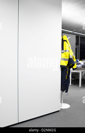 High visibility workers jacket hanging on coat stand  to the side of a large white partition in shared office at night Stock Photo