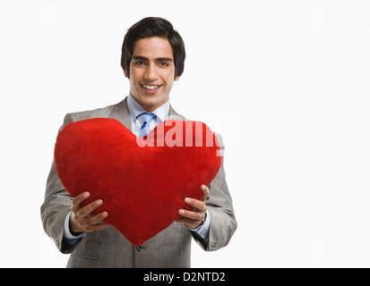 Portrait of a businessman offering a heart shaped cushion and smiling Stock Photo