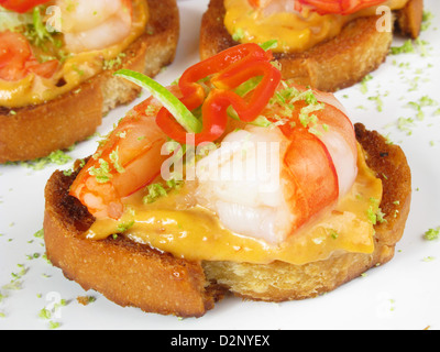 Canapes of tiger prawns on toasted bread with spicy mayonnaise, sliced chillies and lime zest. Stock Photo