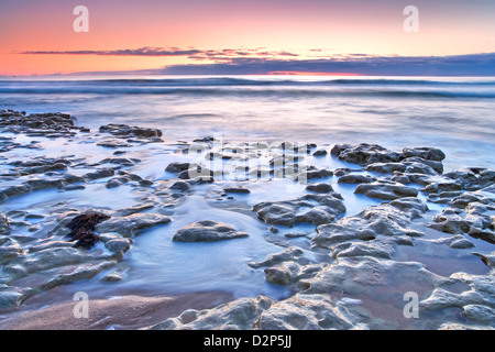 Coastal sunset with waves breaking over the sandy shore. Stock Photo