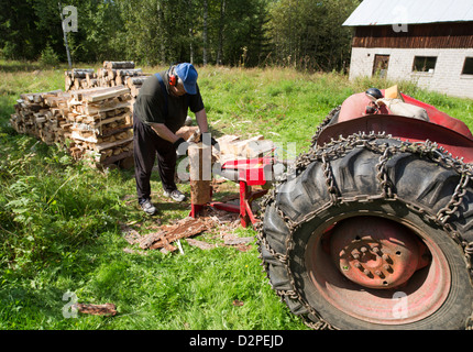 Elderly Caucasian man splitting wood to firewood with tractor powered screw log splitter , Finland Stock Photo