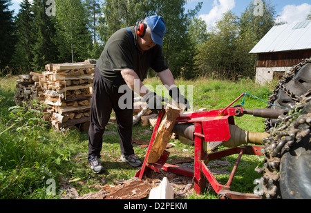 Elderly man splitting wood to firewood with tractor powered screw log splitter , Finland Stock Photo