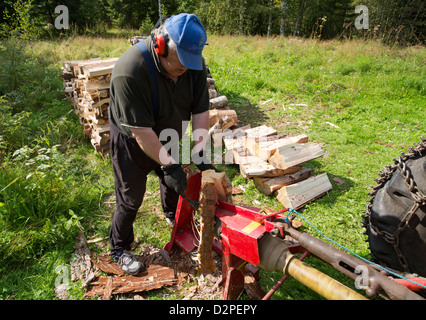 Elderly man splitting wood to firewood with tractor powered screw log splitter , Finland Stock Photo
