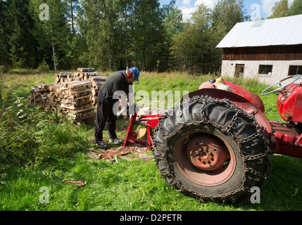 Elderly man making firewood with tractor powered screw log splitter , Finland Stock Photo