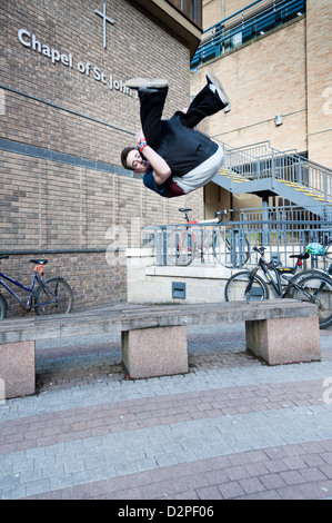 A young man free running or practicing parkour in Cambridge city centre using benches and walls to jump and climb and perform st Stock Photo