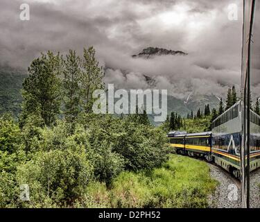 June 28, 2012 - Denali Borough, Alaska, US - An Alaska Railroad passenger train with deluxe McKinley Explorer bi-level dome dining-lounge cars, owned by Holland American Cruise Lines, rounds a curve giving travelers a spectacular view of the storm cloud wreathed summit of Panorama Mountain, 5,538 ft (1,687.98 m) above sea level, as it rises above the evergreen-dominated boreal forest between Denali National Park and Cantwell. (Credit Image: © Arnold Drapkin/ZUMAPRESS.com) Stock Photo