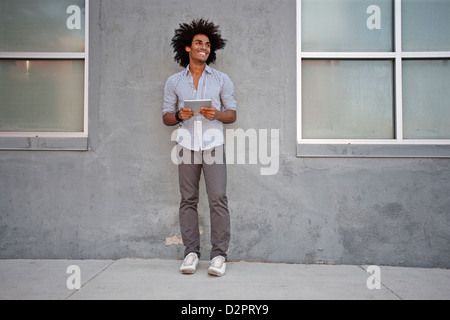 Man using digital tablet and leaning on wall outdoors Stock Photo