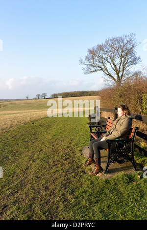 Young woman sits on a bench with a view beside Boudica's Way footpath near Caistor St Edmund Stock Photo