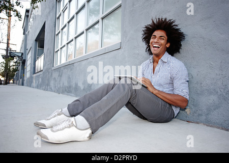 Man using digital tablet and leaning on wall outdoors Stock Photo