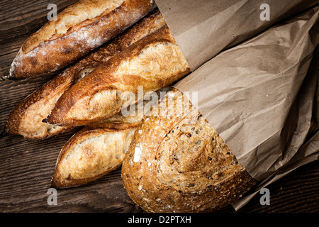Fresh baked rustic bread loaves in paper bags on dark wood background Stock Photo