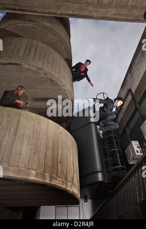 Parkour runners in suits jump from urban building exterior Stock Photo