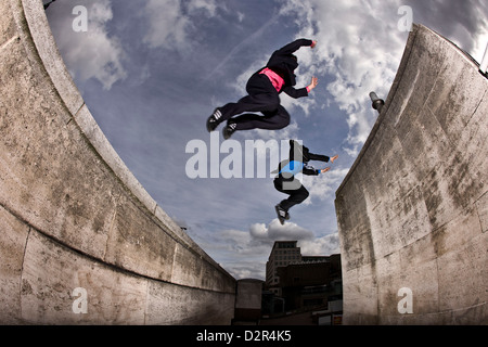 Parkour runners in full suit jumping between concrete roofs Stock Photo