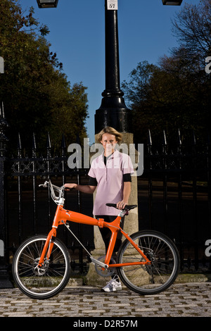 Female cyclist stands with bike at park railings, London Stock Photo
