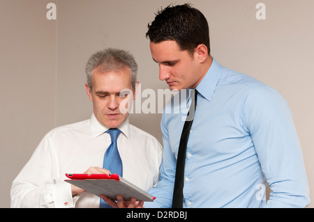 Business colleagues mentor, one young and one older, discuss work using tablet computer. Stock Photo