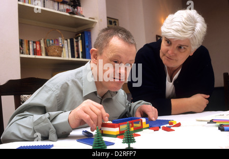 Down syndrome young man with teacher building lego blocks Stock Photo