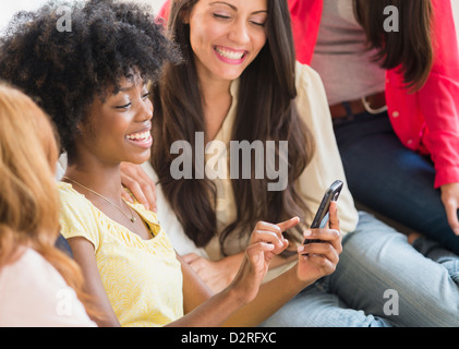 Women using cell phone together on sofa Stock Photo