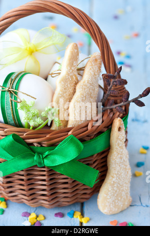 Easter bunny cookies, eggs with ribbon in a basket on an blue wooden board. Stock Photo