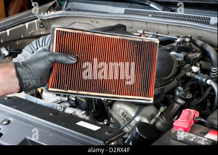 An auto mechanic wearing protective work gloves holds a dirty, clogged air filter Stock Photo