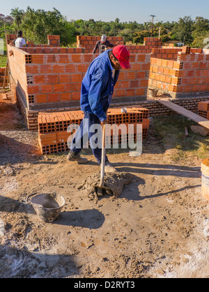 A Hispanic worker mixes mortar on the ground for the construction of a house built with the help of international volunteer labo Stock Photo